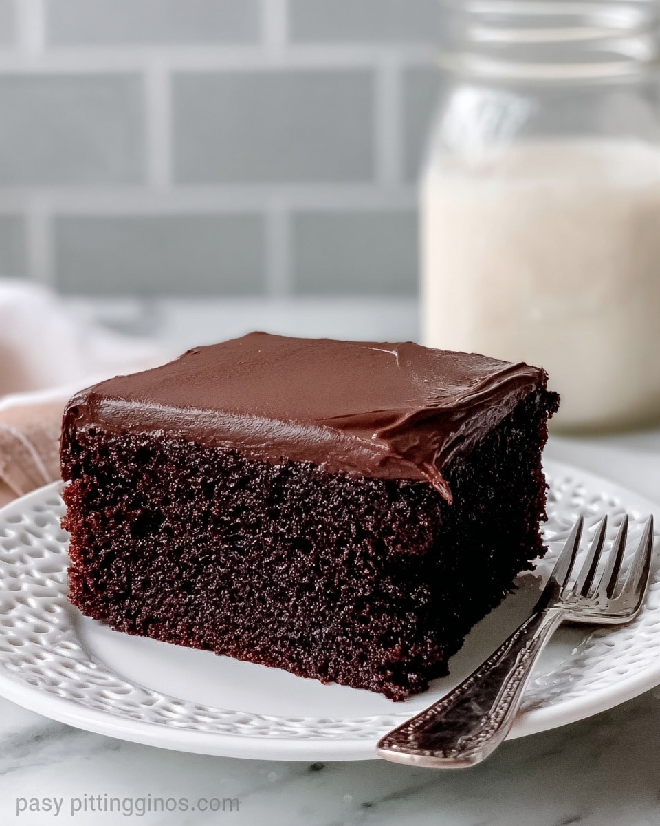A single slice of chocolate cake is shown on a white decorative plate, placed on a white marbled surface. The cake has two layers: a thick, dark brown moist-looking chocolate base and a smooth, glossy chocolate frosting layer on top that covers the entire surface evenly. The texture of the cake looks soft and rich, while the frosting has a creamy, shiny finish. To the right side of the cake slice is a silver fork partially visible. Behind the plate, there is a clear glass jar filled with white cream or milk, adding a light contrast to the dark cake. Photo taken with an iphone --ar 4:5 --v 7