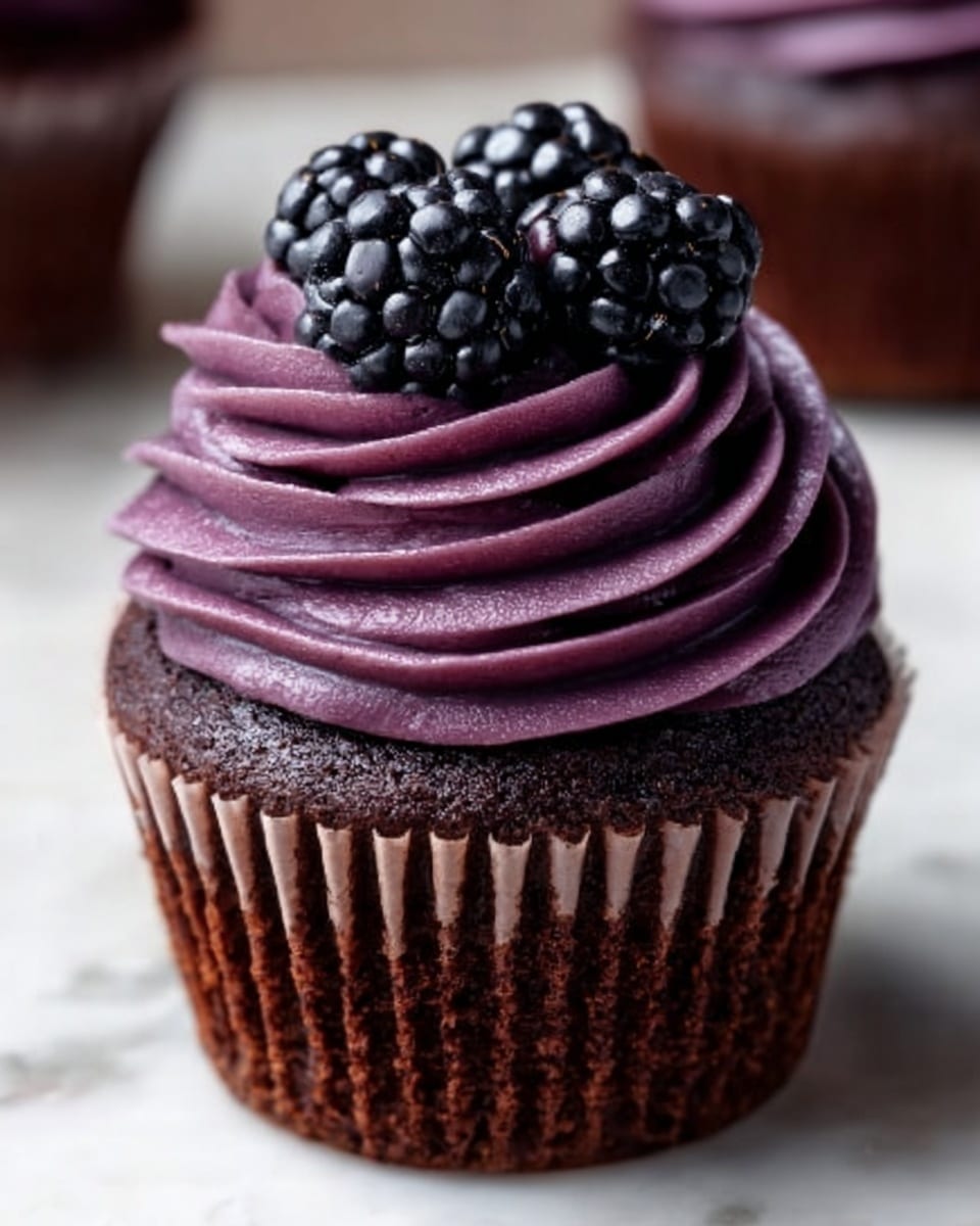 A single chocolate cupcake sits centered, topped with a thick swirl of deep purple frosting that has a smooth, creamy texture. On top of the frosting, there are three shiny blackberries arranged closely together, adding a natural and fresh look. The cupcake liner is dark brown with vertical ridges, showing the contrast between the rich cake and the vibrant frosting. The background has a white marbled texture that highlights the dark and purple colors of the cupcake, making it stand out clearly. photo taken with an iphone --ar 4:5 --v 7