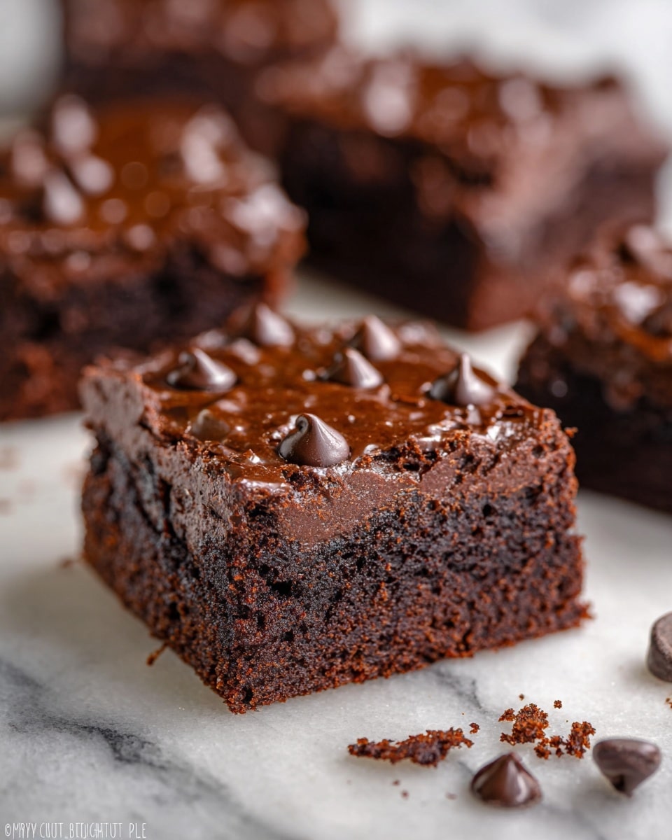 The image shows a close-up view of several rich, moist chocolate brownies. Each brownie has two visible layers: a dense, dark brown cake base with a slightly crumbly texture and a shiny, smooth chocolate ganache-like topping dotted with glossy chocolate chips. The brownies are square-shaped and placed on a white marbled surface, with some chocolate crumbs scattered around. The focus is on one brownie in the center, while others are blurred softly in the background. photo taken with an iphone --ar 4:5 --v 7