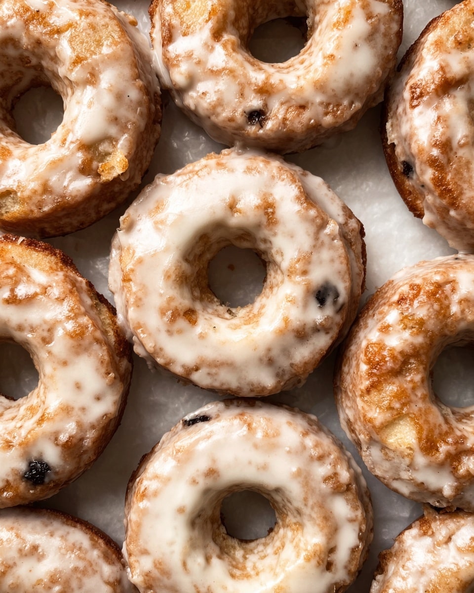 A close-up top view of a group of old-fashioned glazed donuts arranged closely on a white marbled surface, each donut showing one thick layer of light brown dough with a rough texture and cracks, covered in a thin, shiny, white glaze that pools slightly in the crevices, with some small dark spots visible on the donuts themselves, creating a rustic and homemade look, no plate or bowl visible. photo taken with an iphone --ar 4:5 --v 7