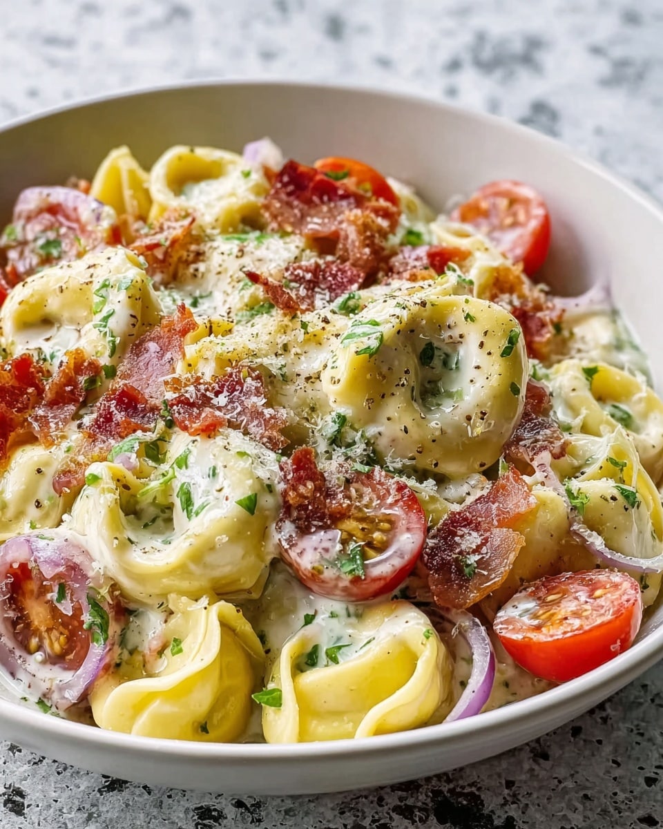 A white bowl filled with a creamy tortellini pasta dish sits on a white marbled surface. The bowl holds several plump yellow tortellini pockets coated with a rich white sauce. Scattered among the pasta are halved bright red cherry tomatoes, thin rings of translucent purple onions, and small pieces of crispy reddish-brown bacon. The dish is sprinkled with grated white cheese, freshly ground black pepper, and finely chopped green herbs, adding contrast and texture to the creamy and colorful mix. The photo has soft natural light and a shallow depth of field that highlights the texture and colors of the dish. photo taken with an iphone --ar 4:5 --v 7