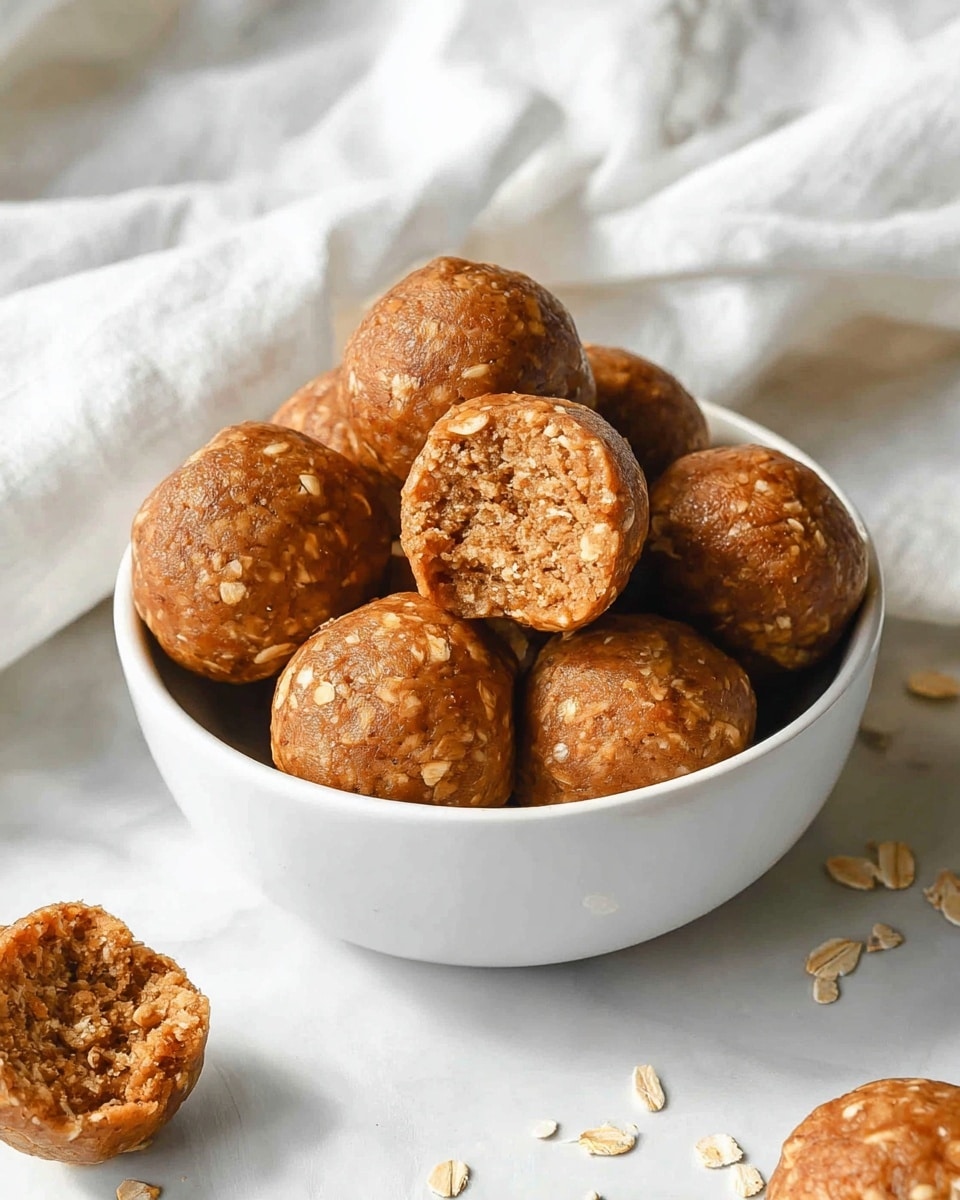A white bowl filled with about eight round oatmeal energy balls that have a light brown color with visible oat flakes mixed inside. One ball is broken open on top, showing a crumbly, dense texture with the oats visible inside. The bowl sits on a white marbled surface, surrounded by a few more energy balls scattered around it, and a soft white cloth in the background. The lighting is soft and natural, highlighting the warm tones and texture of the energy balls. photo taken with an iphone --ar 4:5 --v 7