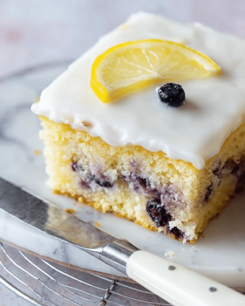 The image shows a square lemon blueberry cake with three layers. The bottom layer is a light yellow sponge cake with visible blueberries inside. The middle layer is a thick white icing that covers the entire top and sides of the cake. On top of the cake is a small yellow lemon slice and a single dark blue blueberry placed near the cut edge. The cake rests on a white marbled surface with a wire cooling rack underneath. A knife with white handles lies next to the cake. The photo taken with an iphone --ar 4:5 --v 7