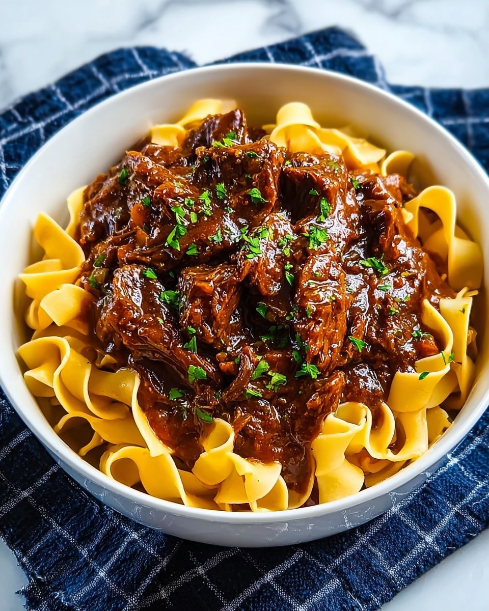 A white bowl filled with wide, yellowish-brown pasta noodles arranged in a loose circular layer at the bottom. On top, there is a thick, rich brown beef stew with visible chunky pieces of tender meat, covered in a glossy sauce. The dish is garnished with small green parsley pieces sprinkled across the stew, adding a fresh contrast in color. The bowl rests on a dark blue cloth with a white grid pattern, placed on a white marbled surface. photo taken with an iphone --ar 4:5 --v 7