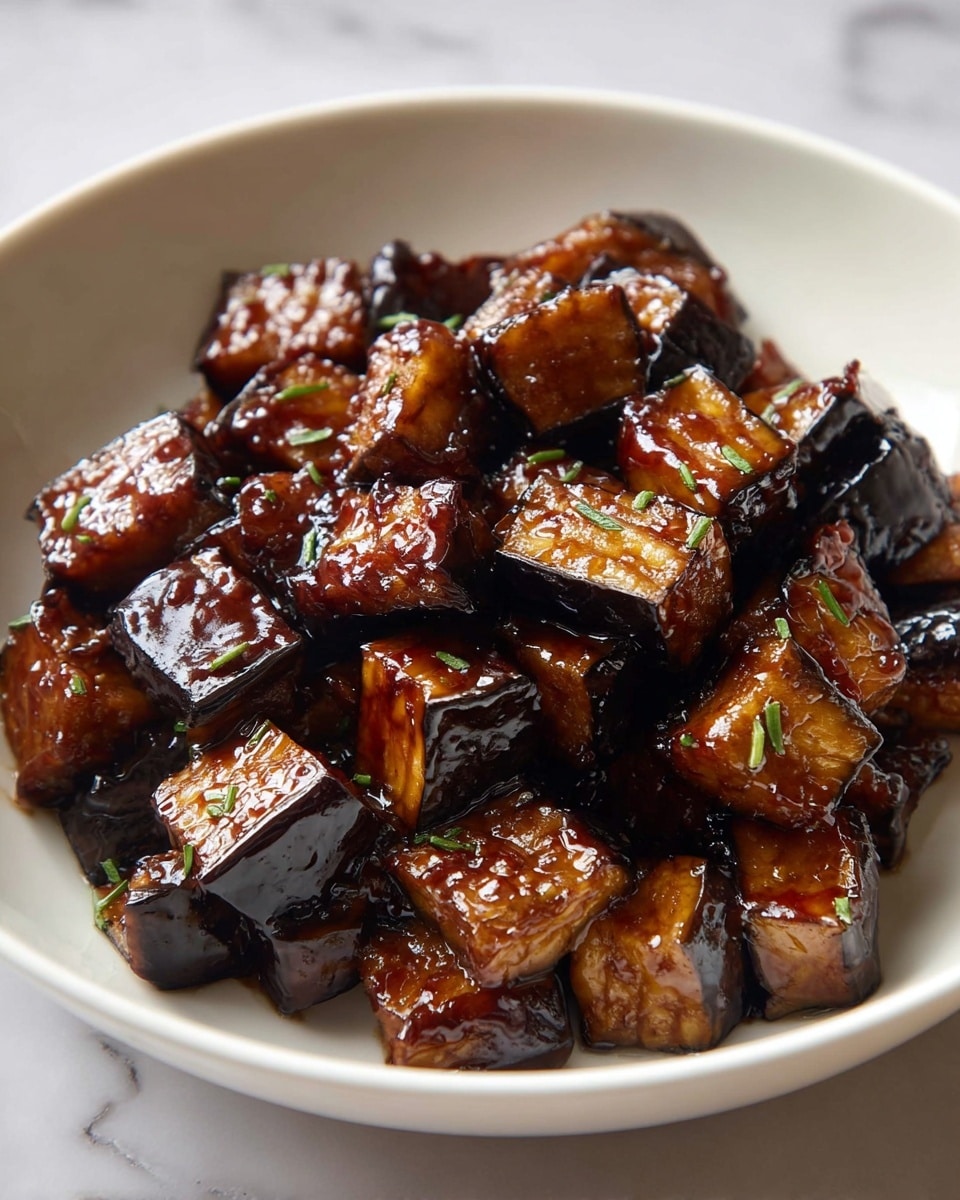 A white bowl filled with about three layers of shiny, dark brown glazed eggplant cubes. The cubes have a mix of deep caramelized brown and black edges with a slightly soft texture inside. The glaze looks sticky and thick, giving a glossy shine to the vegetables. Small green herb pieces are lightly sprinkled on top. The bowl sits on a white marbled surface with soft natural light coming from the side. Photo taken with an iphone --ar 4:5 --v 7