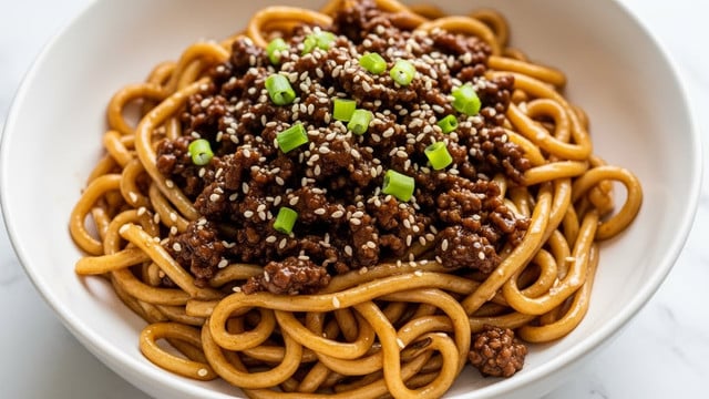 A close-up view of a white bowl filled with glossy, dark brown noodles mixed with small round pieces of cooked shrimp that have a shiny, caramelized coating. The noodles are coated in a thick sauce, giving them a rich brown color with a slight reddish tint. On top, bright green chopped scallions are scattered evenly, adding a fresh contrast to the dish. A pair of wooden chopsticks is lifting a small bundle of noodles from the bowl, showing the sauce's shine and the noodle's texture. The surface beneath the bowl is a white marbled texture. Photo taken with an iphone --ar 4:5 --v 7